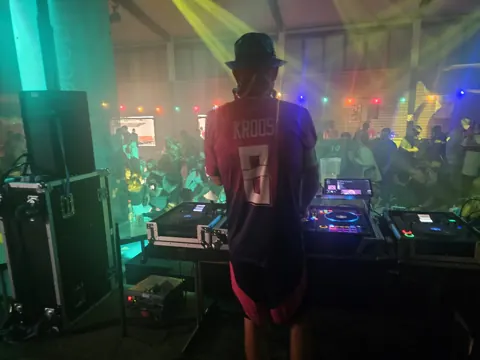 DJ-Pult, Publikum und gelbe Lichtstrahlen im Veranstaltungssaal