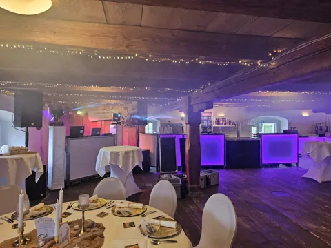 Veranstaltungsraum mit DJ-Aufbau, farbiger Beleuchtung und Bar