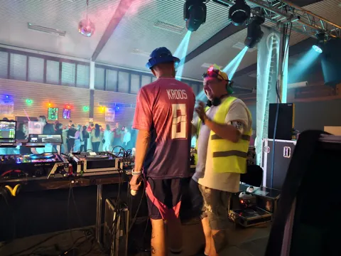Zwei Personen am DJ-Pult mit Lichtstrahlen im Saal