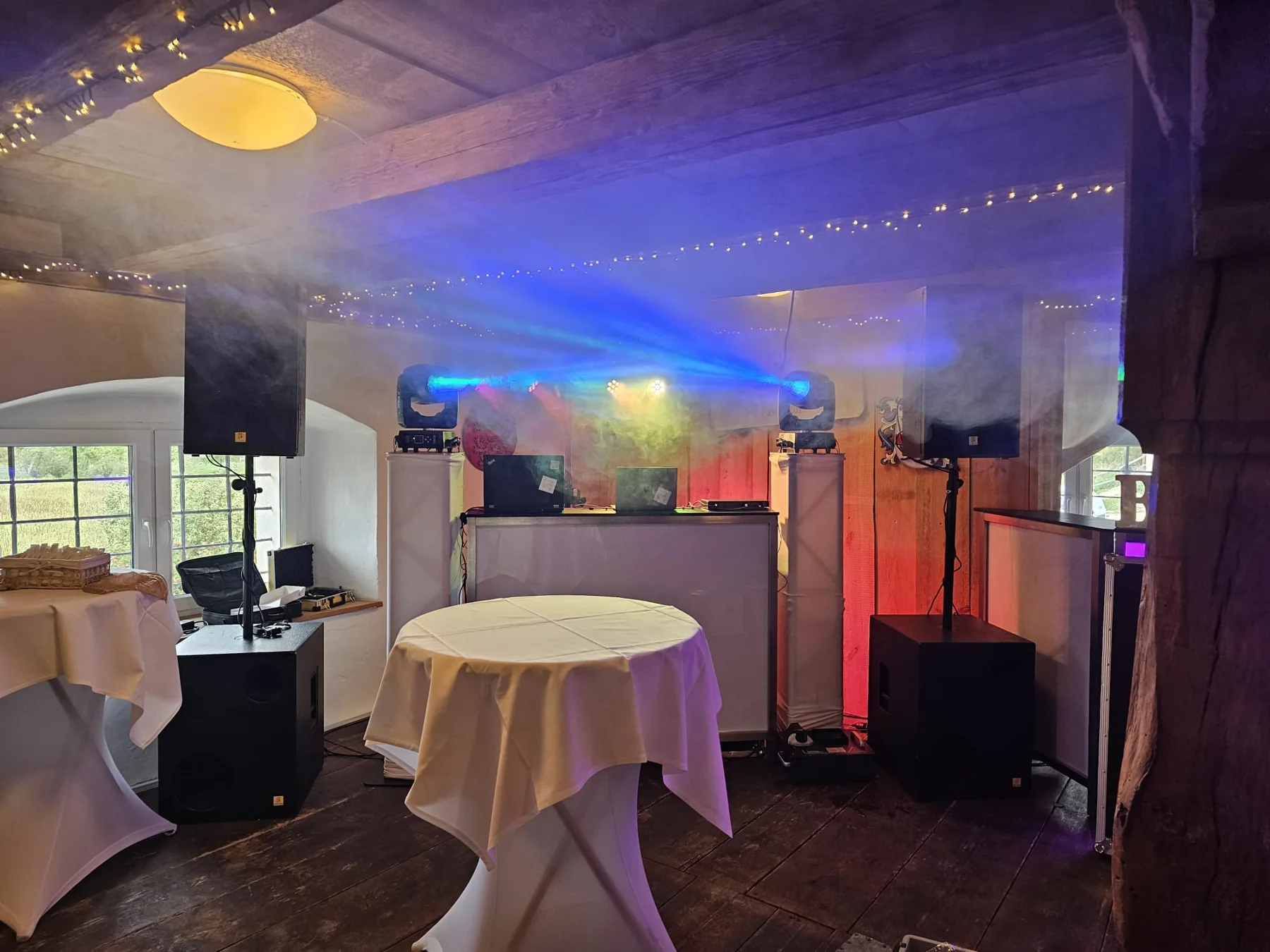 Reale Veranstaltungsaufnahme: DJ-Aufbau mit Lautsprechern, Lichtstrahlen und weiß verkleideten Technikpodesten